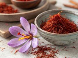 Rustic bowl filled with dried saffron threads with fresh pink flowers photo