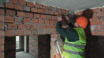 Construction worker adjusting reinforcement on a brick wall, Worker in a safety vest and hard hat securing reinforcement on bricks. video