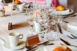 A beautifully set table featuring wine glasses and a name tag. The white tablecloth is adorned with pink napkins, complemented by pink and white flower decorations. photo