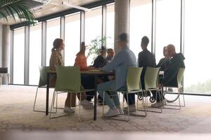 A diverse business team, working urgently around a conference table, collaborates on a meeting while their director, seated in a wheelchair, waits for their input photo