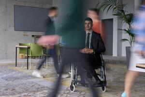 A businessman in a wheelchair navigating through a busy office, surrounded by his colleagues who are actively engaged in their work and collaboration photo