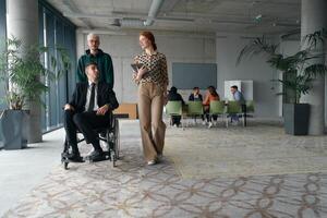 A diverse and multicultural business team collaborates in the office while their colleagues, including a director in a wheelchair and his friend, share a lighthearted moment, fostering an atmosphere photo