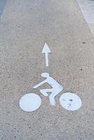 The image displays a white bicycle lane sign on gray concrete. This sign marks the designated area for cyclists, promoting safety and encouraging proper lane usage for all road users. photo