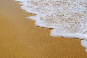 Close-Up of a Soft Wave Gently Lapping at the Sandy Beach Under a Clear Blue Sky with Clouds photo