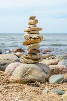 This image showcases a carefully balanced stack of smooth, round stones set against a serene beach backdrop. The calm blue sea gently laps at the shore, while the sky remains clear and inviting. photo