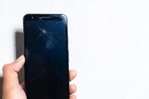 A person holding a black smartphone with a cracked screen photo