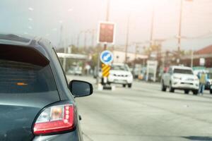Rear side view of gray car. Body of car with dust of rain on the glass. wtih turn on brake light and turn signal light. Conretet road with traffic signal. Opposit of road with cars line up in a queue. photo