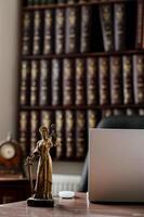 A refined legal workspace with a grand bookshelf packed with law books, a well organized desk, and a bronze statue of Themis holding her scales and sword photo