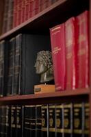 A bookshelf filled with Greek-language law books, neatly arranged alongside a classical bust of Alexander the Great. photo