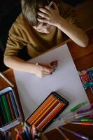The boy is surrounded by art supplies, staring at a blank sheet of paper, deep in thought. photo