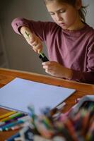 The girl leans over the table, deep in creative thought, with art tools around her. photo