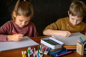 The siblings lean over their papers, lost in creative thought, with crayons scattered around. photo
