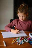 Surrounded by colors, the girl holds a crayon, pondering her next idea. photo
