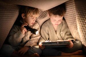 Childhood adventure two boys reading a book under a cozy blanket fort, lit by a flashlight photo