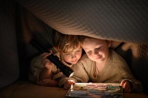 Two young brothers huddled under a blanket, enjoying a bedtime story illuminated by a flashlight. photo