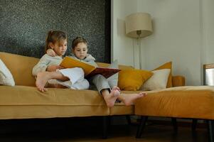The siblings sit on the sofa, reading a book, lost in the world of imagination. photo