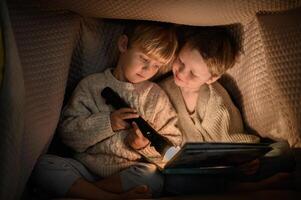Two little boys reading a book under a blanket with a flashlight, creating a cozy, secretive atmosphere. photo
