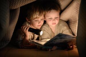 Two small boys sharing a magical moment, reading together under a blanket with soft flashlight glow. photo
