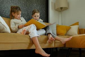 A girl and boy share a cozy afternoon on the couch, reading their favorite book together. photo