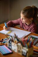 A girl sits at a table with crayons and markers, thinking about what to draw photo