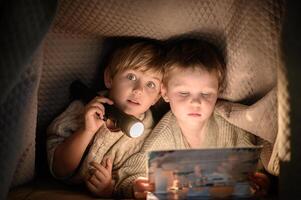 Two kids immersed in a story, sitting under a blanket with a flashlight in the dark. photo