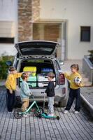 The open trunk of a car is surrounded by four kids organizing vibrant suitcases and scooters for their adventure. photo