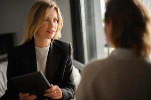 A business meeting between two women in a sleek office space. One woman is presenting ideas while the other listens attentively, both focused on the task at hand. photo