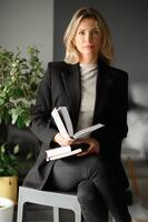 A professional blonde psychologist with a beautiful smile, seated at her desk in an office lined with books. photo