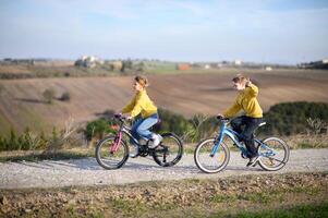 Two kids cycle along a rural path, surrounded by fields, on a bright and sunny day. photo