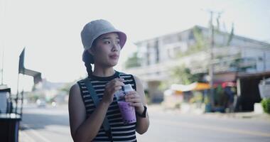 Beautiful woman stands on the sidewalk admiring the city view while drinking a refreshing sweet drink. video
