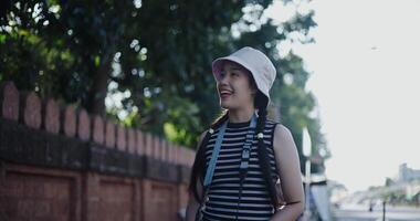 Mano bajo ángulo ver disparo. hermosa asiático mujer en casual ropa es teniendo divertido tomando fotos de el ciudad ver con un cámara en un acera en el ciudad. video