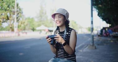 Beautiful woman in casual clothes is having fun taking photos of the city view with a camera on a sidewalk in the city. video