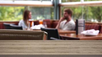 Empty wooden table with background of a couple sitting chatting and eating in a restaurant, looping to show video