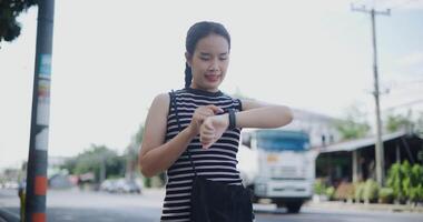 Handheld low angle view shot, Young Asian woman standing outdoors using a map app on her smart watch and enjoy looking around at a cityscape. video