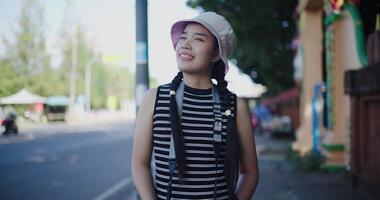 Beautiful woman in a striped tank top and hat stands outdoors on a sidewalk, holding a camera, looking at photos with enjoyment. video