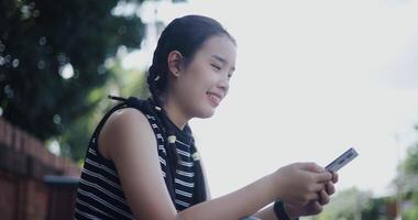 Handheld low angle view shot, Young Asian woman sits on the sidewalk enjoying the city view and looking at something on her mobile phone. video