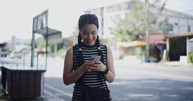Handheld shot, Young Asian woman standing outdoor enjoying the view of the city while using a map app to find directions on mobile phone. video
