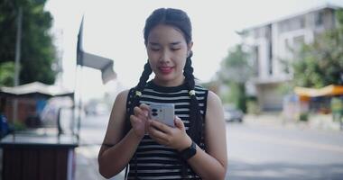 Handheld shot, Young Asian woman standing outdoor enjoying the view of the city while using a map app to find directions on mobile phone video