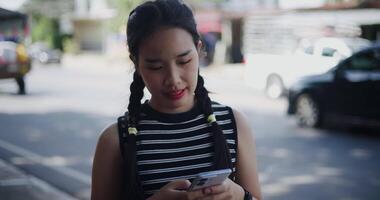 Handheld shot, Asian woman standing outdoors enjoying the view of the city while using a map app to find directions on mobile phone. video
