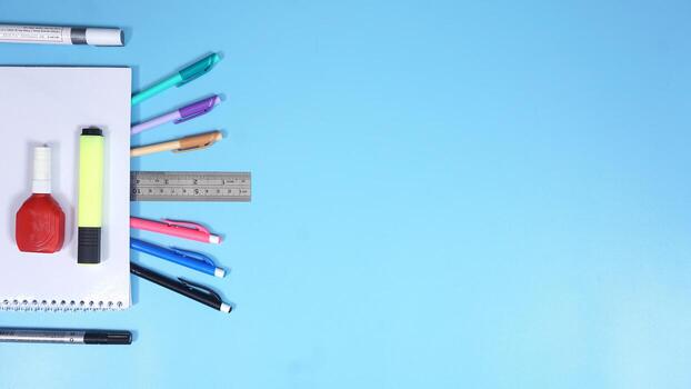 Various Color of Pens with Other Stationery and Notebook on Blue Background photo