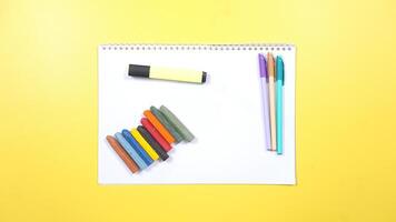 Various Color of Pens and Crayons with Highlighter and Notebook on Yellow Background photo