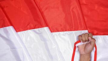 Red and White National Flag of Indonesia as Background for Copy Space with Man's Hand Holding Red and White Ribbons photo