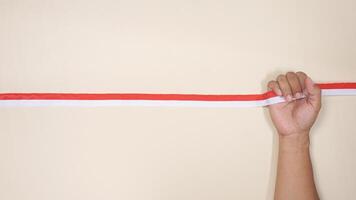 Man's Hand Holding Red and White Ribbons as Symbol of Indonesia National Flag on Light Background photo