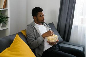 African American man sits alone on the couch and enjoying popcorn while watching television and streaming service photo