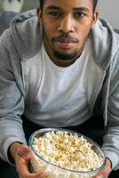 African American man sits alone on the couch and enjoying popcorn while watching television and streaming service photo