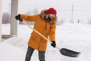 A man cleans and clears the snow in front of the house on frosty day. Cleaning the street from snow on a winter day. Snowfall and severe snowstorm in winter. photo