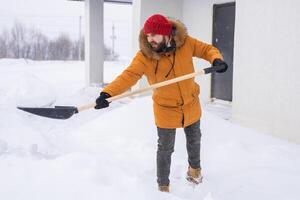 A man cleans and clears the snow in front of the house on frosty day. Cleaning the street from snow on a winter day. Snowfall and severe snowstorm in winter. photo