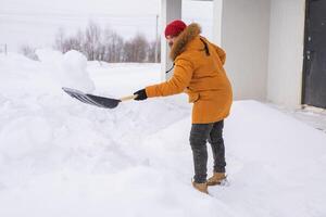 A man cleans and clears the snow in front of the house on frosty day. Cleaning the street from snow on a winter day. Snowfall and severe snowstorm in winter. photo