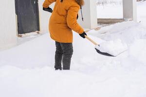 Young man clearing snow in his backyard village house with shovel close-up. Remove snow from the sidewalk. photo