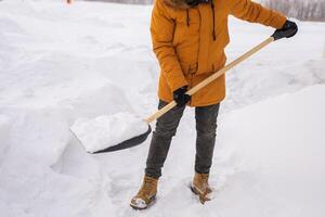 Close-up Young man clearing snow in his backyard village house with shovel. Remove snow from the sidewalk. photo